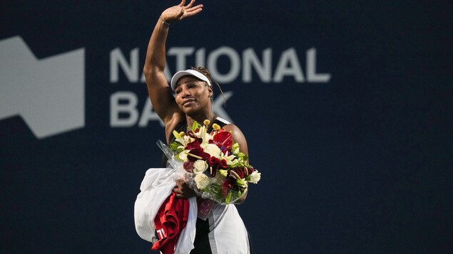 Une joueuse de tennis salue la foule d'une main et tient un bouquet de fleurs de l'autre.