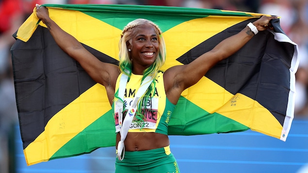 Une sprinteuse de la Jamaïque pose fièrement avec sa médaille au coup en tenant son drapeau national dans son dos. 