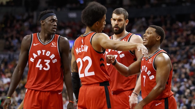 Deux joueurs discutent d'une stratégie tandis que deux autres prêtent l'oreille. Ils sont tous vêtus de l'uniforme rouge des Raptors de Toronto.