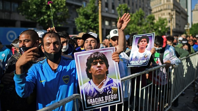 Des supporteurs en file montrent des photos de Diego Maradona.