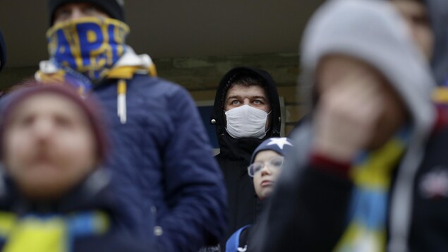Des supporteurs du FC Bate, dont un qui porte un masque protecteur, assistent à une rencontre.