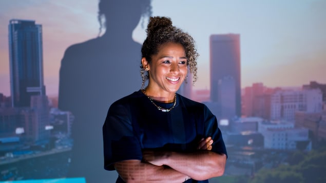 Elle croise les bras devant une vue de la ville de Winnipeg.