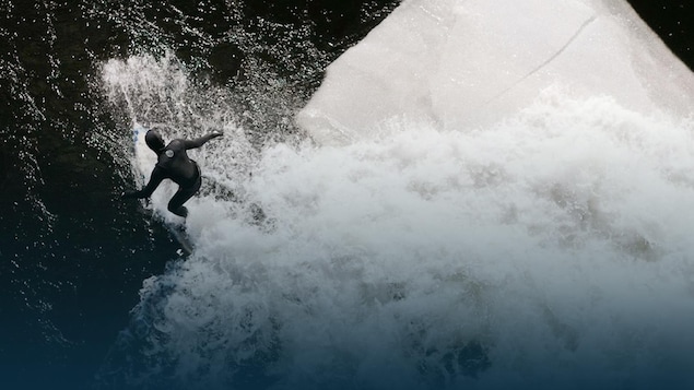 Un surfeur se tient debout sur sa planche près d'un gros morceau de glace.