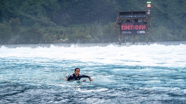 Une athlète est à plat ventre sur sa planche dans l'eau.