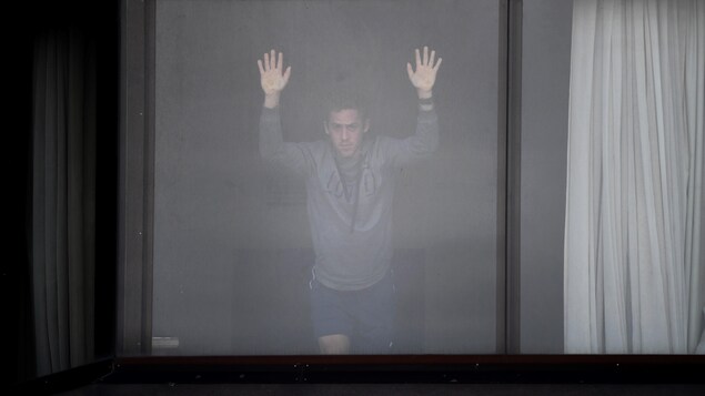 Un homme regarde par la fenêtre de sa chambre d'hôtel.