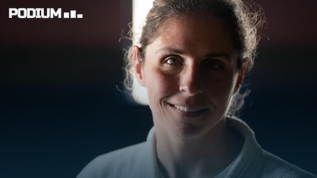 Une femme en judogi blanc sourit. installée devant un fond noir.