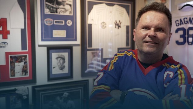 Un homme qui porte un chandail de hockey regarde la caméra en souriant.