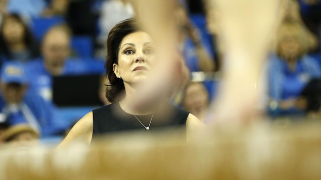 Une entraîneuse de gymnastique regarde le programme de l'une de ses athlètes à la poutre.