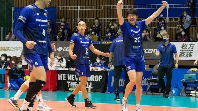 Des joueurs célèbrent un point marqué au volleyball sous l'œil attentif de leur entraîneur.