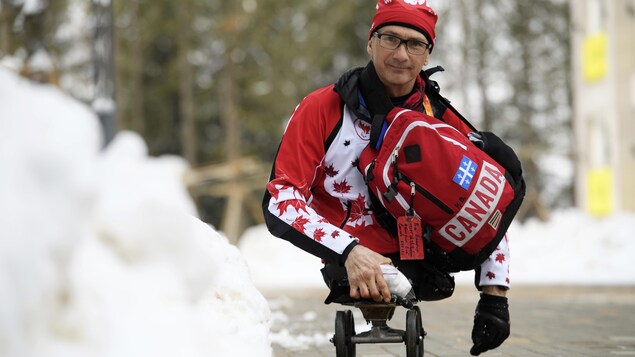 Yves Bourque sourit à la caméra. Il est en train de se déplacer sur sa planche à roulettes. Il porte un sac à dos aux couleurs du Canada.