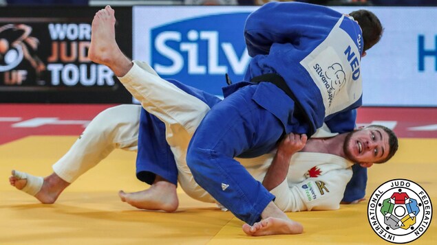 La judoka canadien Zachary Burt, en blanc, est immobilisé au sol par Néerlandais Jesper Smink, en bleu.