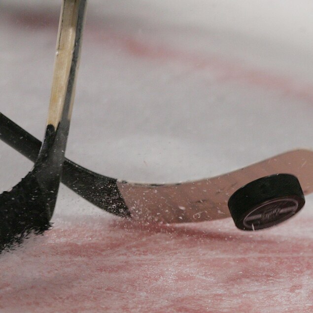 Deux bâtons de hockey et une rondelle, lors d'une mise au jeu. 