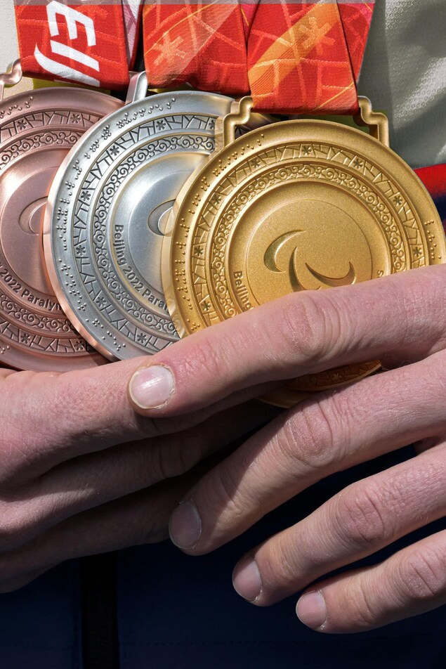 Un athlète tient trois médailles entre ses mains, une en or, une en argent et une en bronze.