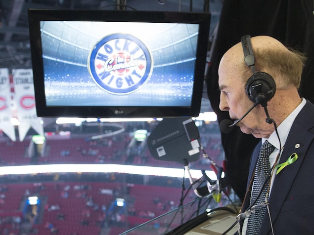 Un homme âgé sur la galerie de presse du Centre Bell, regarde la glace en bas. Il porte des écouteurs et un micro. Il est écrit Hockey Night in Canada sur un écran.