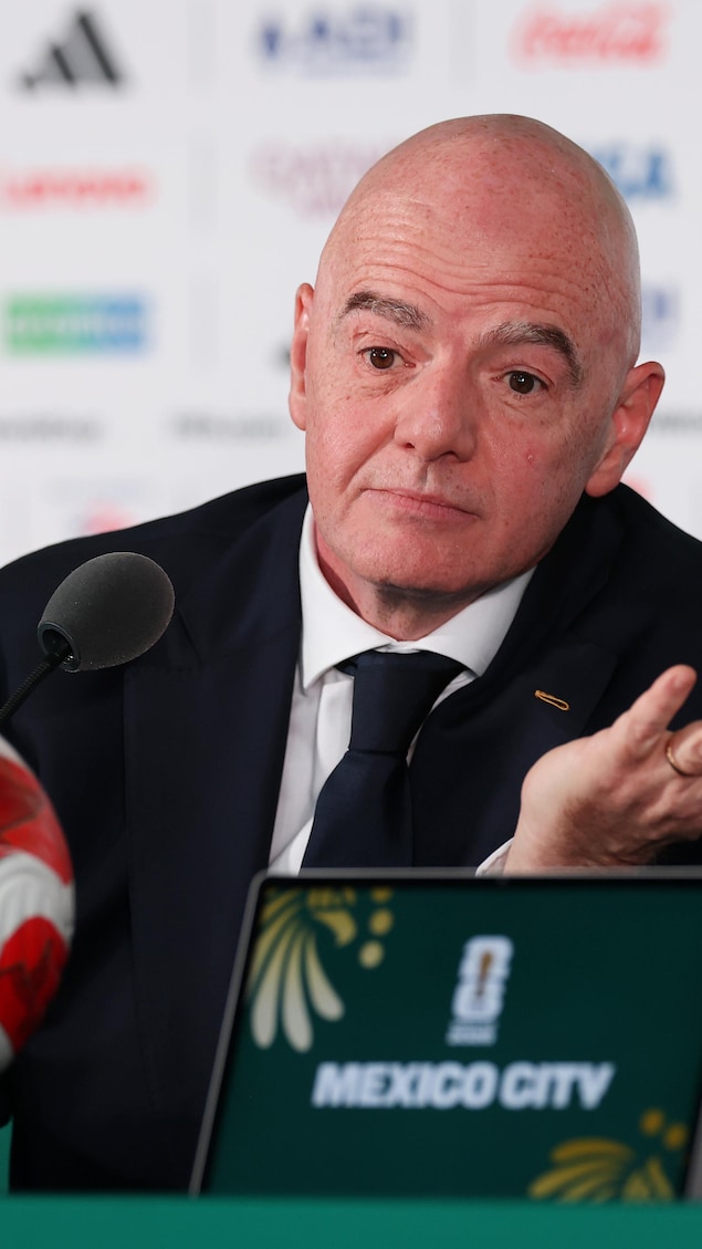 Un homme est derrière un micro, il y a un ballon de soccer devant lui.