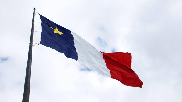Plan rapproché d'un grand drapeau de l'Acadie qui flotte au sommet d'un mât.