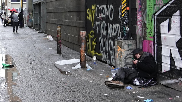 Un homme étendu près de poubelles dans une ruelle.