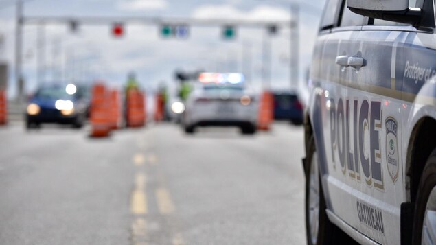 La mise au point sur le mot "police" sur la porte d'une auto-patrouille avec en arrière plan un barrage routier.