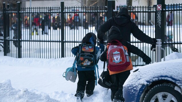 Des enfants marchent dans la neige avec leur parent vers la cours d'école. 