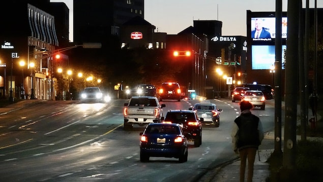 Circulation automobile et une personne qui marche sur le trottoir en début de soirée sur la rue Main à Moncton.