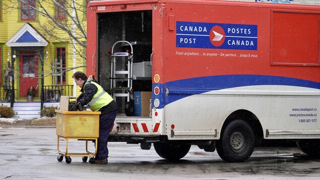 Un travailleur manipule des colis derrière un camion de Postes Canada.