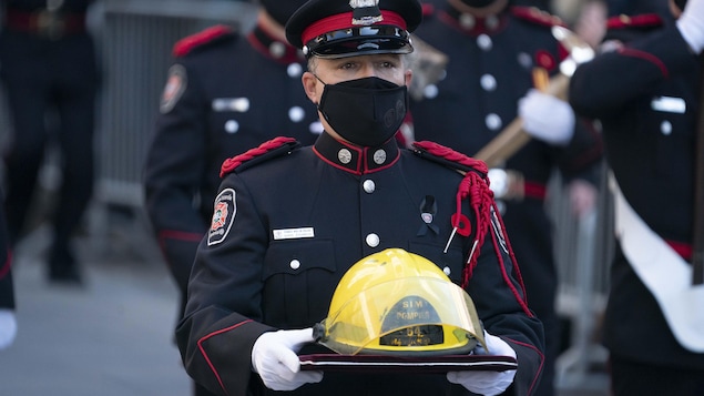Un pompier en uniforme tient un casque jaune entre ses mains.
