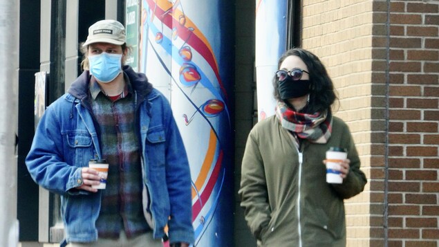 Des passants dans la rue, café à la main et masque sur le visage.