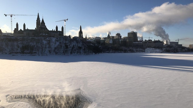 Le parlement d'Ottawa, en hiver, au bord d'une rivière recouverte de neige.