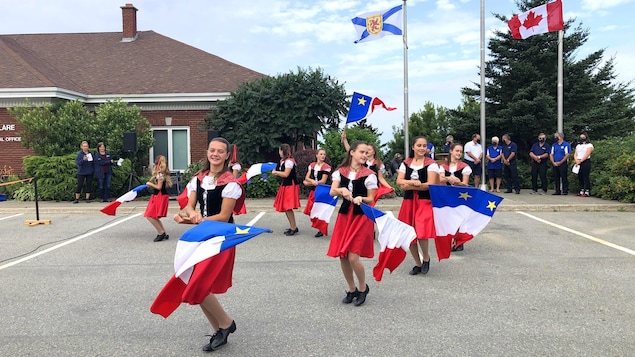 Des jeunes à l'extérieur agitent des drapeaux de l'Acadie.