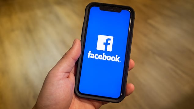 Une main tenant un téléphone avec le logo de Facebook.