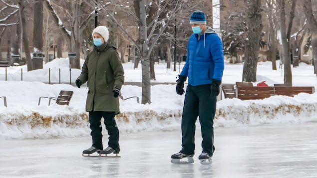 Deux personnes à Regina, en Saskatchewan, font du patin en hiver tout en portant un masque pour se protéger de la COVID-19.