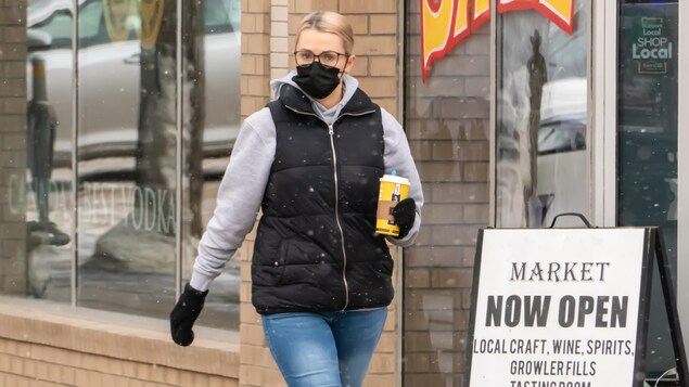 Une femme marche dans une rue de Saskatoon et porte un masque.