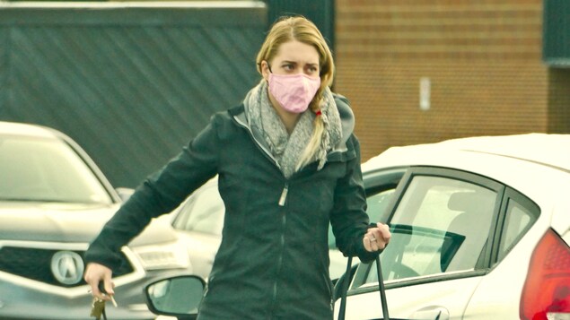 Une femme en manteau d'hiver et portant un masque traverse un stationnement.
