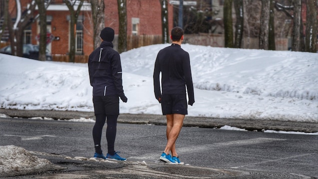 Deux personnes en tenue d'entraînement se tiennent à un coin de rue enneigé.