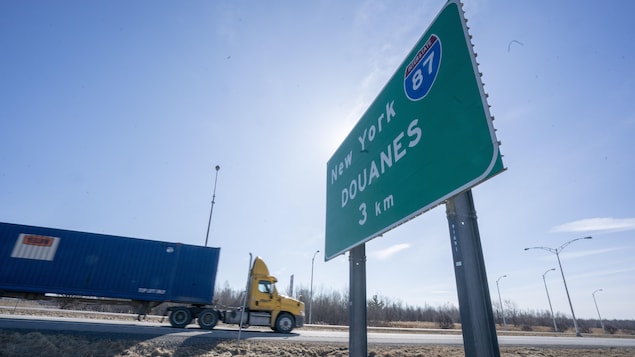 Un camion semi-remorque circule sur une route avec en avant-plan une pancarte annonçant les douanes et l'I-87 dans l'État de New York.