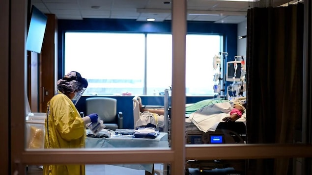 Une infirmière vêtue d'équipements de protection personnelle est dans la chambre d'un patient.