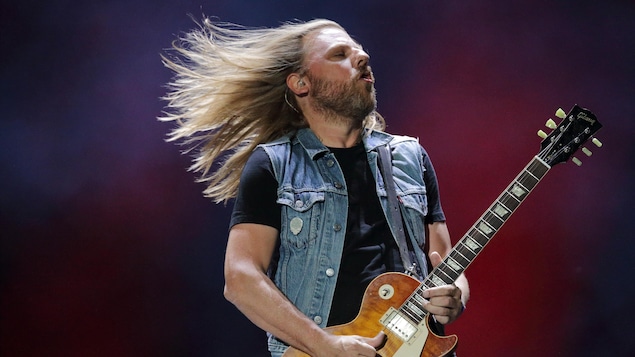 Un guitariste en pleine performance sur scène, les cheveux au vent.