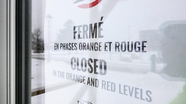 Une affiche sur une porte vitrée. Il est écrit : « Fermé en phases orange et rouge ».