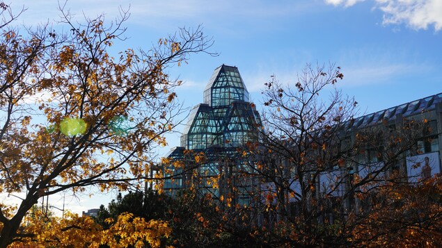 L'édifice vitré du Musée derrière les feuilles oranges d'un arbre en automne