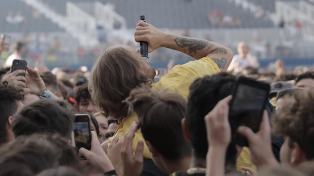 Le chanteur se fait porter par la foule. Il chante en même temps. Les spectateurs le filment avec leur cellulaire. 