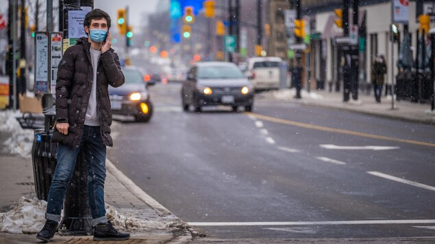 Un homme portant le masque parle dans son téléphone cellulaire dehors.