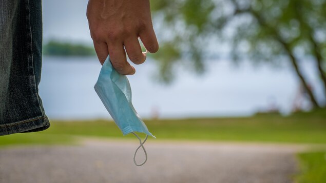 Gros plan sur un masque chirurgical dans la main d'une personne près d'un point d'eau.