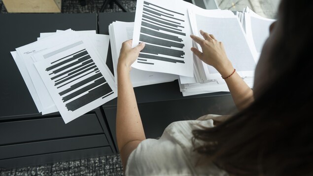 On voit quelqu'un feuilleter des documents caviardés.