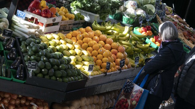 Une femme devant des étals de fruits et légumes.