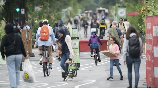 Des passants, dont des enfants, une femme portant le hijab et un homme à vélo, sont dans une rue de Montréal.