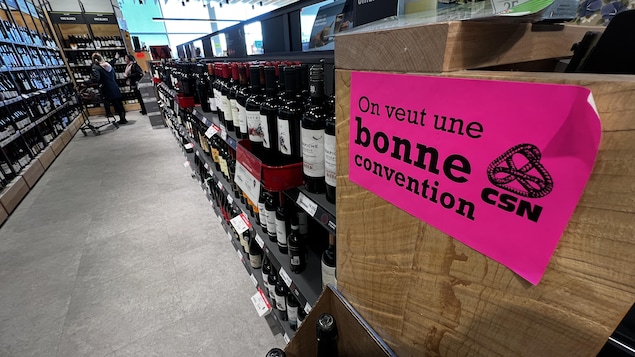 Un autocollant du syndicat CSN disant : « On veut une bonne convention » collé au bout d'une rangée de bouteilles de vin dans une succursale de la SAQ.