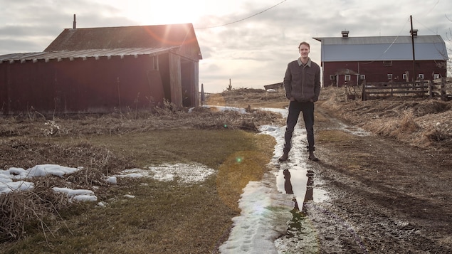 Pierre Sabourin sur la ferme de ses amis dans un sentier entre deux bâtiments.