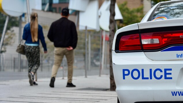 Un couple marche près d'une voiture de police.