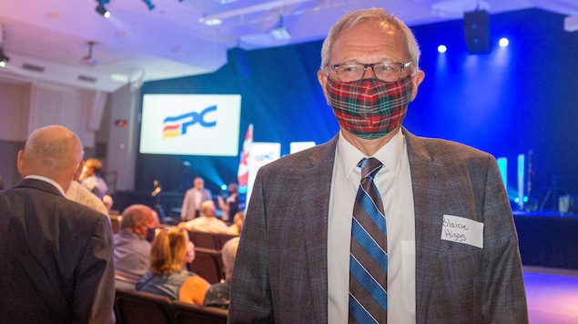 Blaine Higgs en complet et cravate porte sur le nez et la bouche un masque non médical en tissu à carreaux rouges et verts.