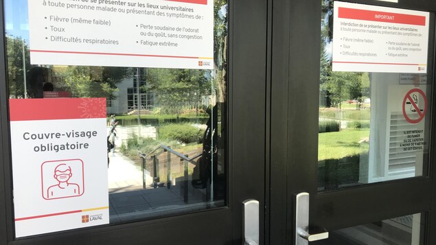 Des affiches sont collées aux portes de l'Université Laval informent les étudiants que le port du masque est obligatoire et qu'il est interdit de se présenter sur les lieux s'ils éprouvent des symptômes de COVID.